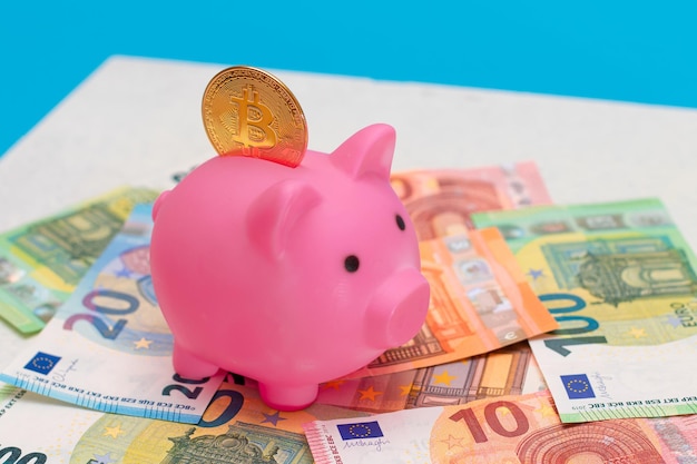 Pink piggy bank with bitcoin coin on the euro banknotes