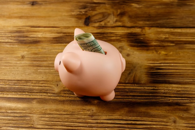 Pink piggy bank with one dollar bill on a wooden desk Saving money concept