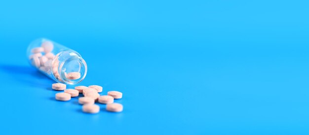 Pink pills are poured out of a glass bottle on a blue background Vitamin B complex copy space