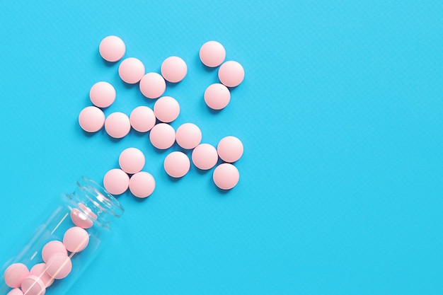 Pink pills are poured out of a glass bottle on a blue background Vitamin B complex copy space