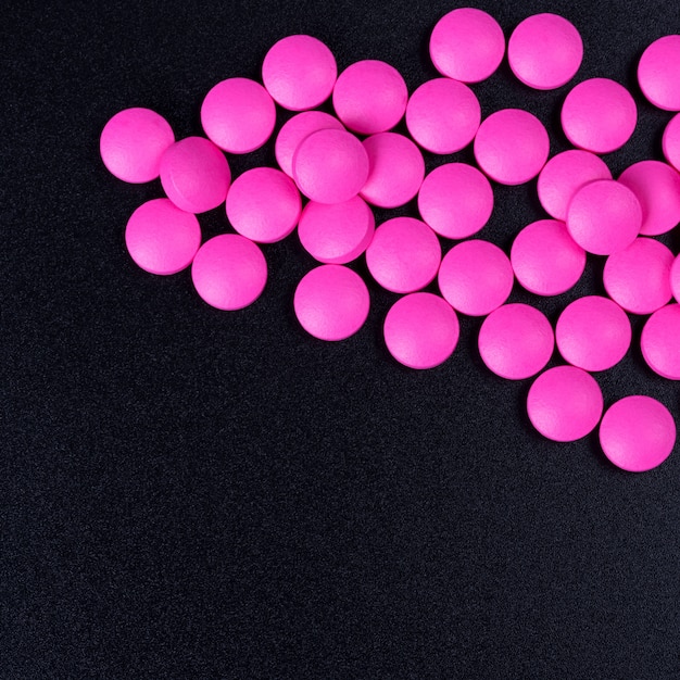 Розовые таблетки разбросаны на черном фоне.