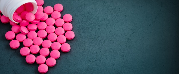 Фото Розовые таблетки разбросаны от банки на сером фоне.