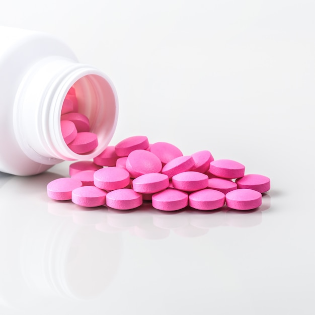 Pink pills are scattered from a jar on white 