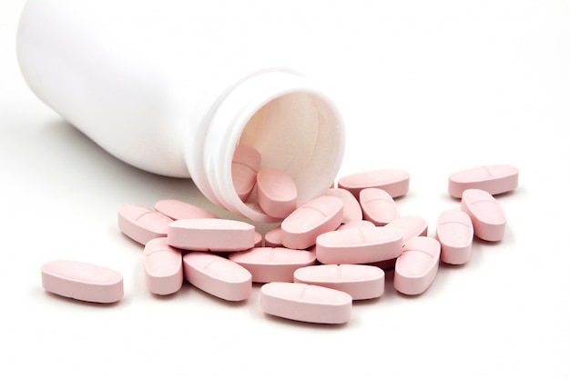 Pink pills an pill bottle on white background