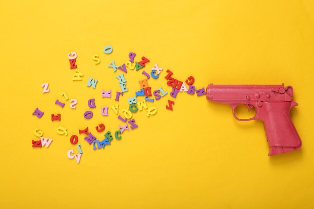 Pink pistol gun shooting letters on yellow background Creative minimalism layout Concept art Flat lay Top view