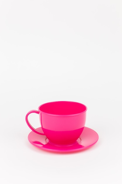 Tazza di plastica rosa con piattino su sfondo bianco