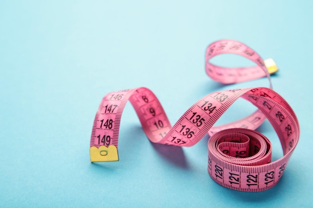 Pink plastic measure tape with metric scale over on blue background