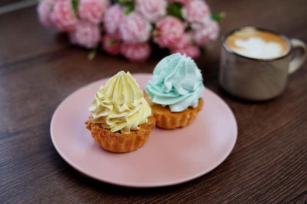 A Pink Plate with birthday Capcakes sits on a wooden table. A beige cup of cappuccino