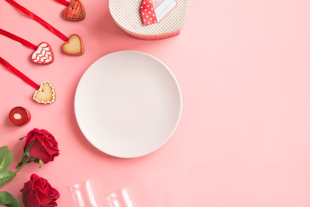 Розовая тарелка с печеньем и розы на день Святого Валентина на розовом фоне.