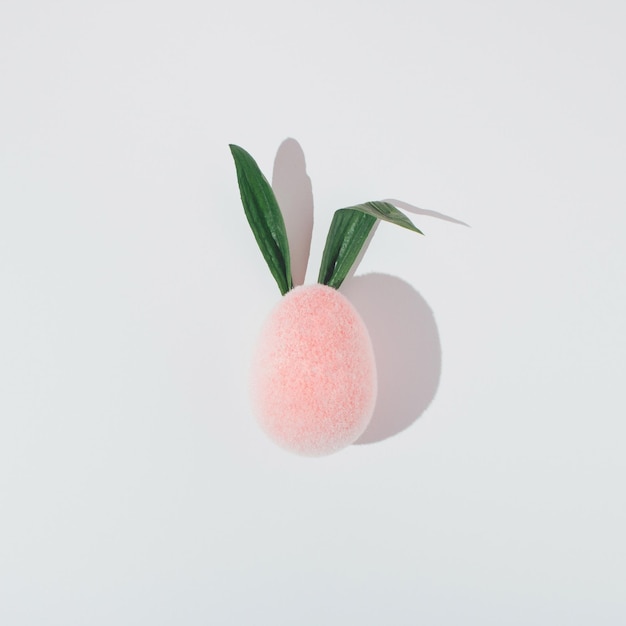 Pink plush egg with fresh leaves as bunny ears on white background