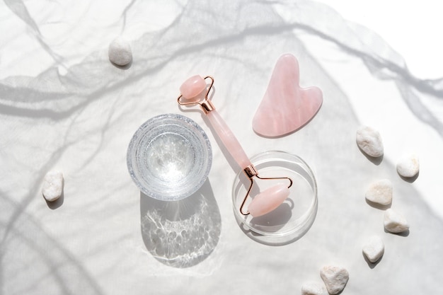 Pink quarts face roller gua sha stone serum capsules in chemical glass dish hexagons Beauty facial massage Natural cosmetics laboratory Off white flat lay in off white and pink
