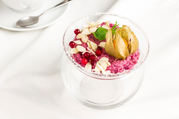 Pink raw dessert mousse ice cream with berries and nuts in glass jar on white table