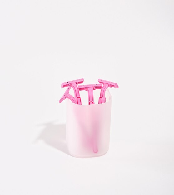 Pink razors stand in a white cup isolated on white background Shaving accessories Hygienic supplies