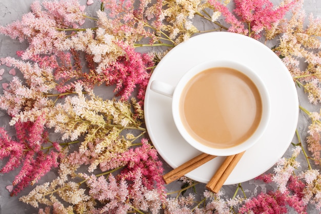 Pink and red astilbe flowers and a cup of coffee on a gray concrete background. top view.