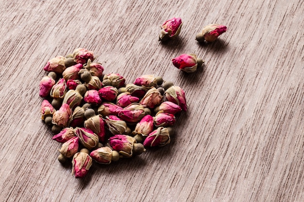 Pink red dried rose buds heart shaped on old wooden table with copyspace.