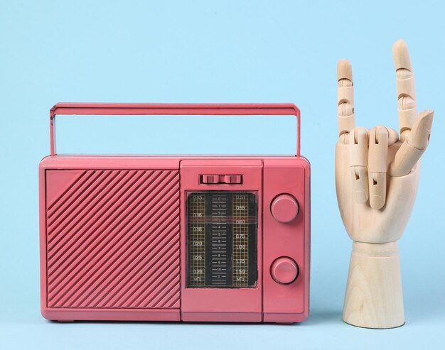 Pink retro radio receiver and wooden hand showing rock gesture on blue background