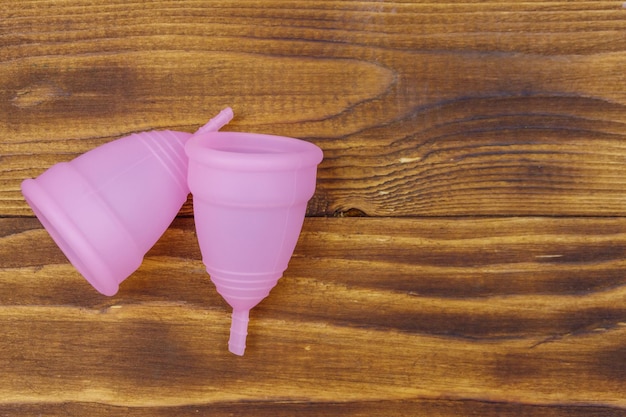 Pink reusable silicone menstrual cups on wooden background top\
view copy space concept of feminine hygiene gynecology and\
health