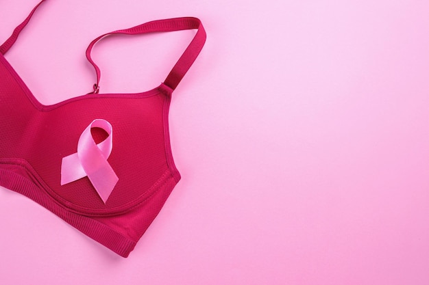 Photo pink ribbon attached to brassiere on pink background with empty space
