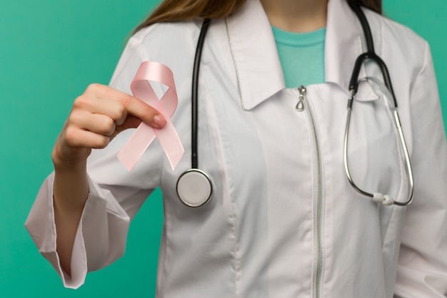 Nastro rosa per la consapevolezza del cancro al seno nella mano del medico della donna sullo spazio blu