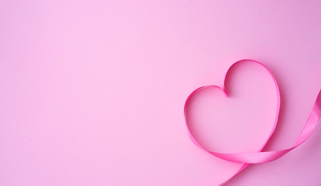 Pink ribbon folded in the shape of a heart on a pink background Love and valentines day concept