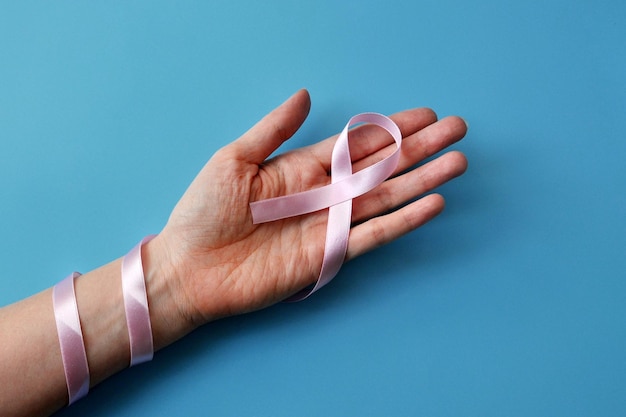 Pink ribbon in the hands of a woman. A symbol of the fight against breast cancer