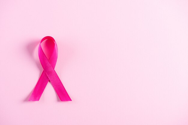 Pink ribbon on pink paper background for supporting breast cancer awareness