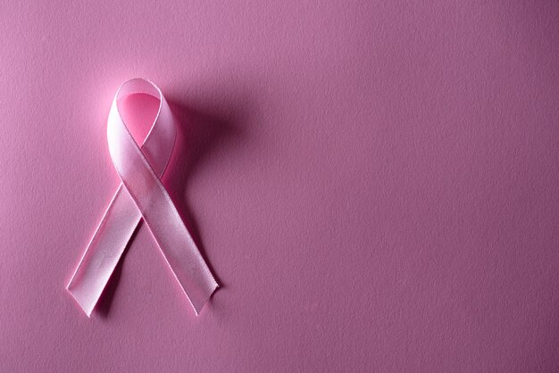 Pink ribbon on pink pastel paper for supporting breast cancer awareness.