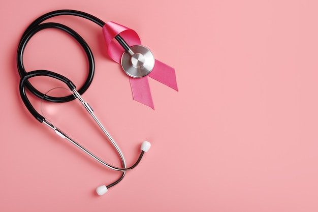 ピンクの背景にピンクのリボンと聴診器。乳がん啓発の概念
