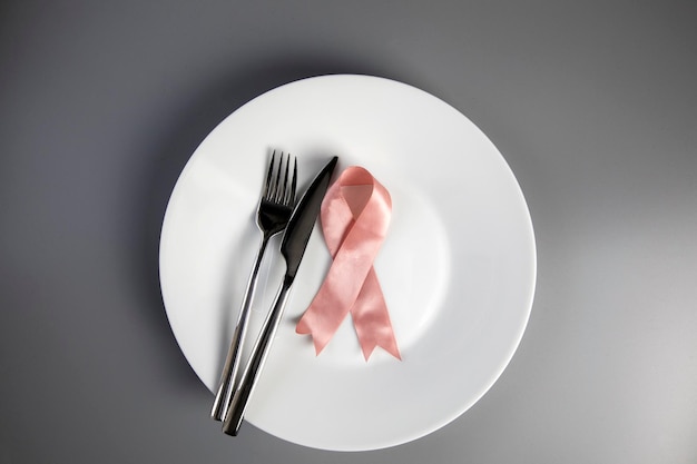 Pink ribbon on white plate with knife and fork breast cancer awareness concept top view medical heal...