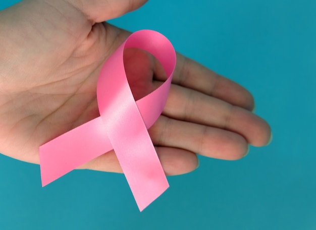 Pink ribbon on a woman's hand on and blue background