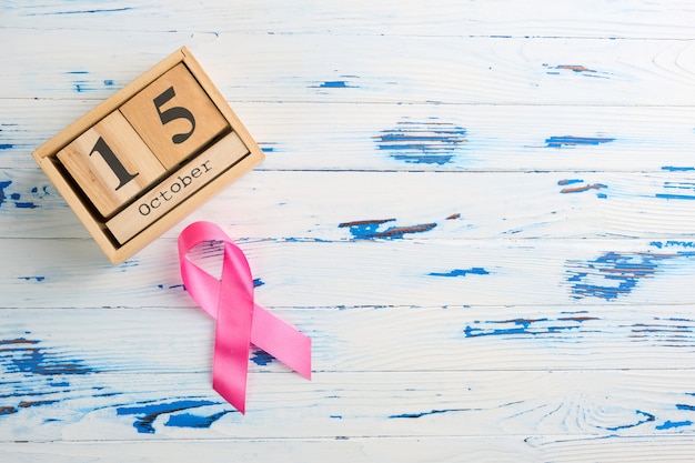 Photo pink ribbon and wooden cube calendar set for october 15 on a wooden table.