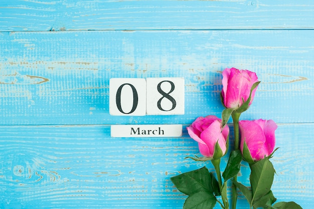 Photo pink rose flower and 8th march calendar on blue wood table background with copy space for text. love, equal and international women day concept