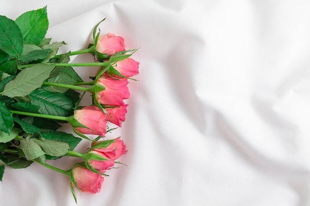 Pink rose with green leaves among the folds of a white textured textile roses on bed romantic concept