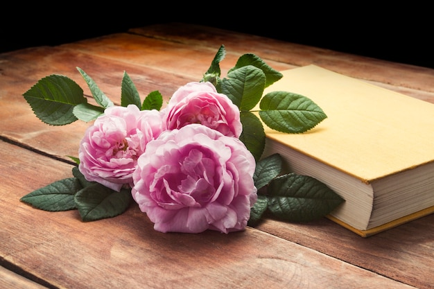 Pink roses and book with a yellow cover on a wooden surface