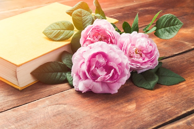 Pink roses and book with a yellow cover on a wooden surface