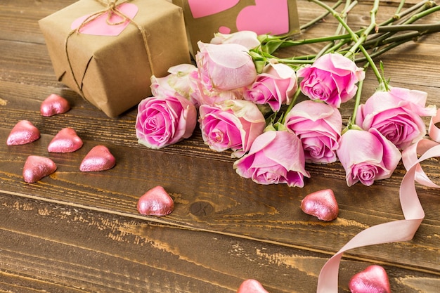 Pink roses and gift wrapped in recycled paper on rustic wood table.