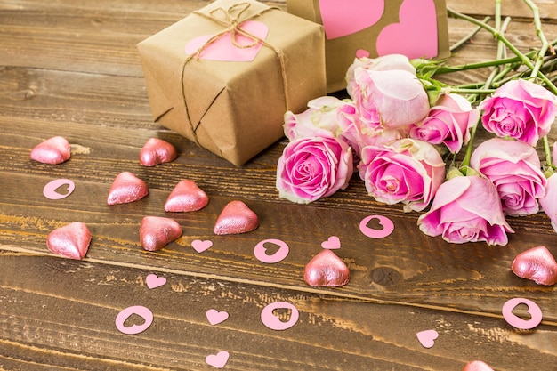 Pink roses and gift wrapped in recycled paper on rustic wood table.