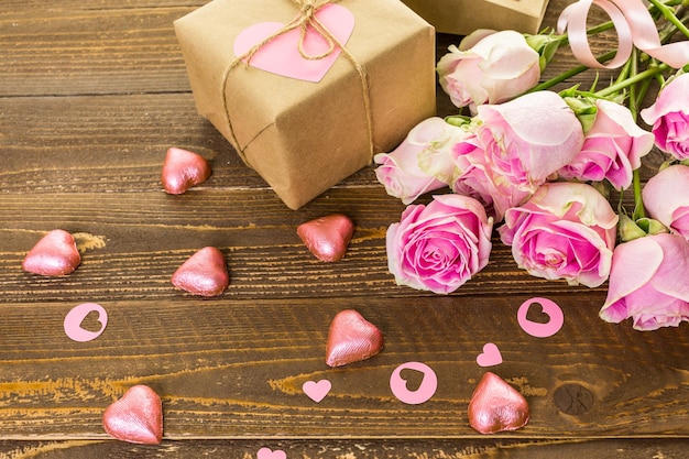 Pink roses and gift wrapped in recycled paper on rustic wood table.