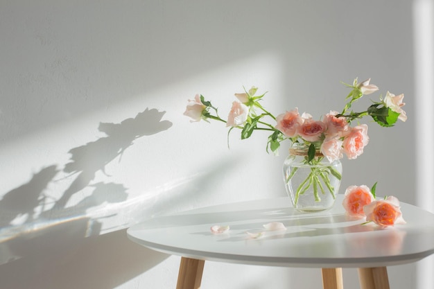 Pink roses in glass jar on white modern table on background white wall