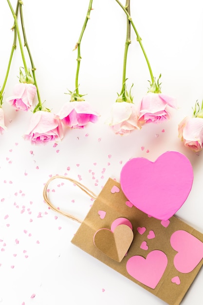 Pink roses and hand crafted gift bag on a white background.