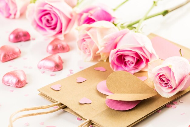 Pink roses and hand crafted gift bag on a white background.