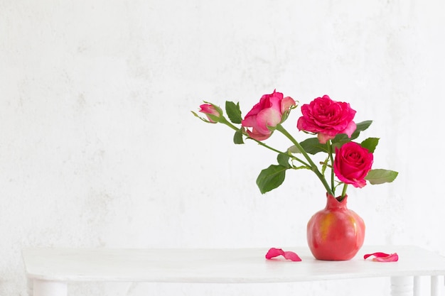 背景の古い白い壁にピンクの花瓶にピンクのバラ