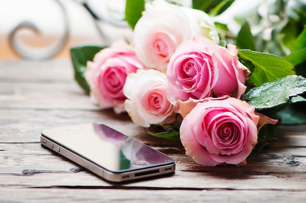 Pink roses and smartphone on the wooden table