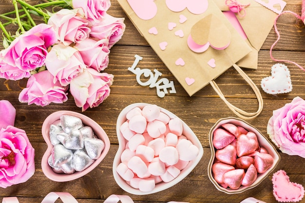 Pink roses with chocolates on rustic wood table.