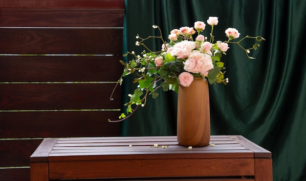 розовые розы с плющом в вазе на деревянной полке на задней стене и зеленой занавеске