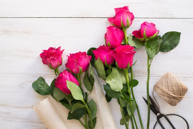 Foto rose rosa, carta da imballaggio, spago e forbici vintage sulla tavola di legno bianca