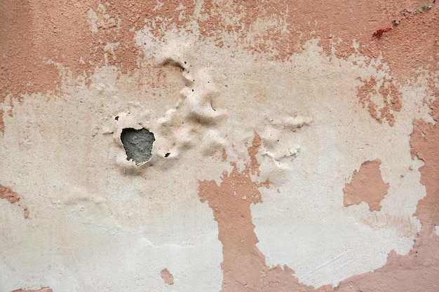 Pink rough painted wall of the house with pieces of fallen plaster pink city wallpaper