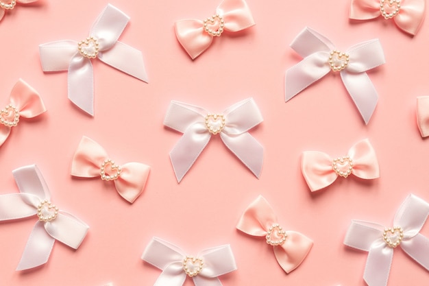 Pink satin bows with pearl hearts pattern on pink surface.