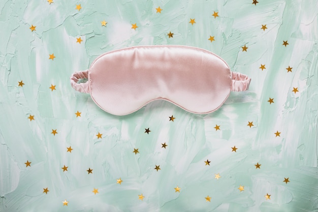 Foto maschera per dormire in raso rosa e coriandoli di stelle in lamina d'oro sul tavolo verde