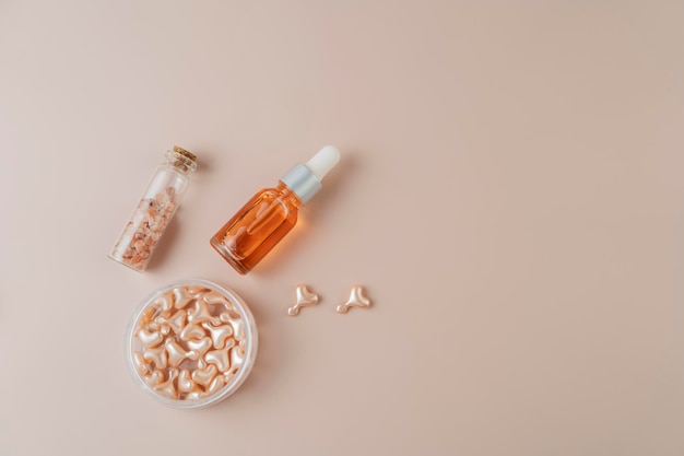 A pink sea salt in a small glass bottle a face serum in pink capsules lying on a pink background